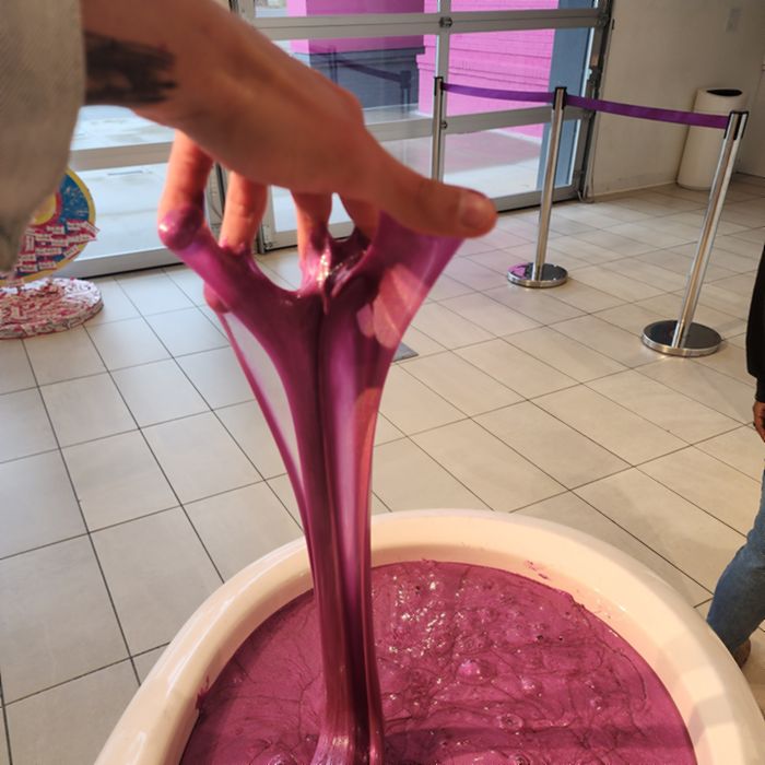 A hand stretching a long ribbon of magenta glitter slime up out of a tub.