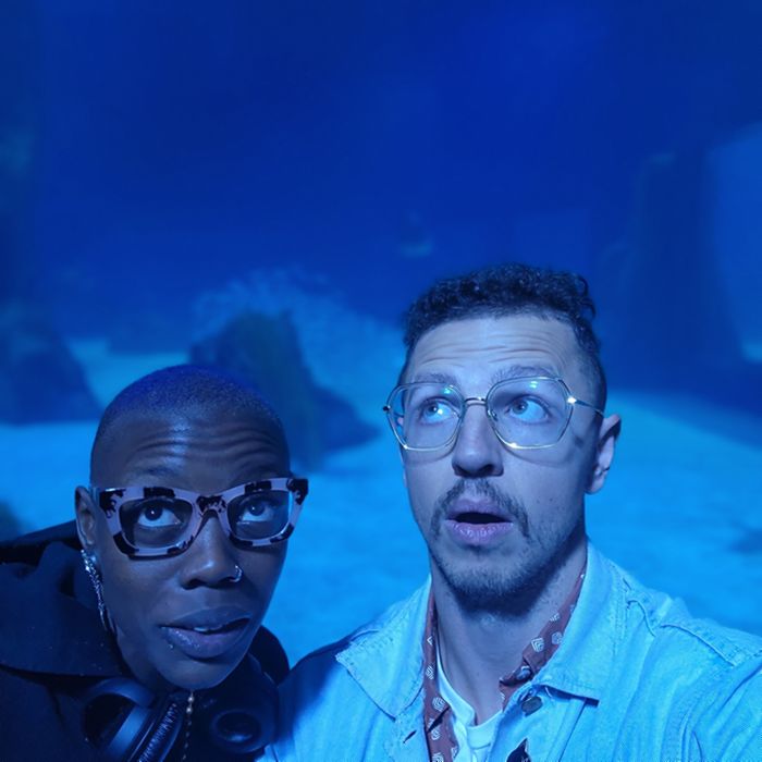 Imani and Julian looking up in wonder, lit blue by a huge aquarium tank.