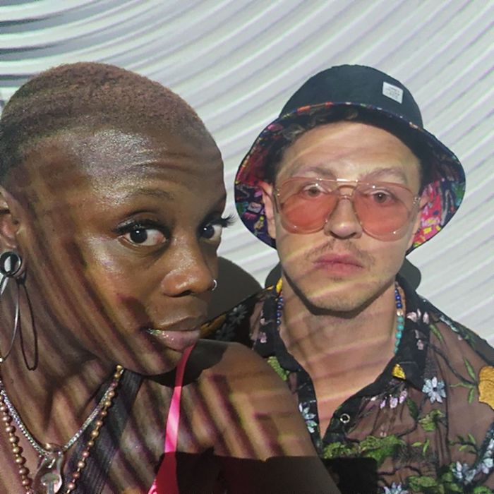 Imani and Julian side by side, patterned light projected across them at an evening event.
