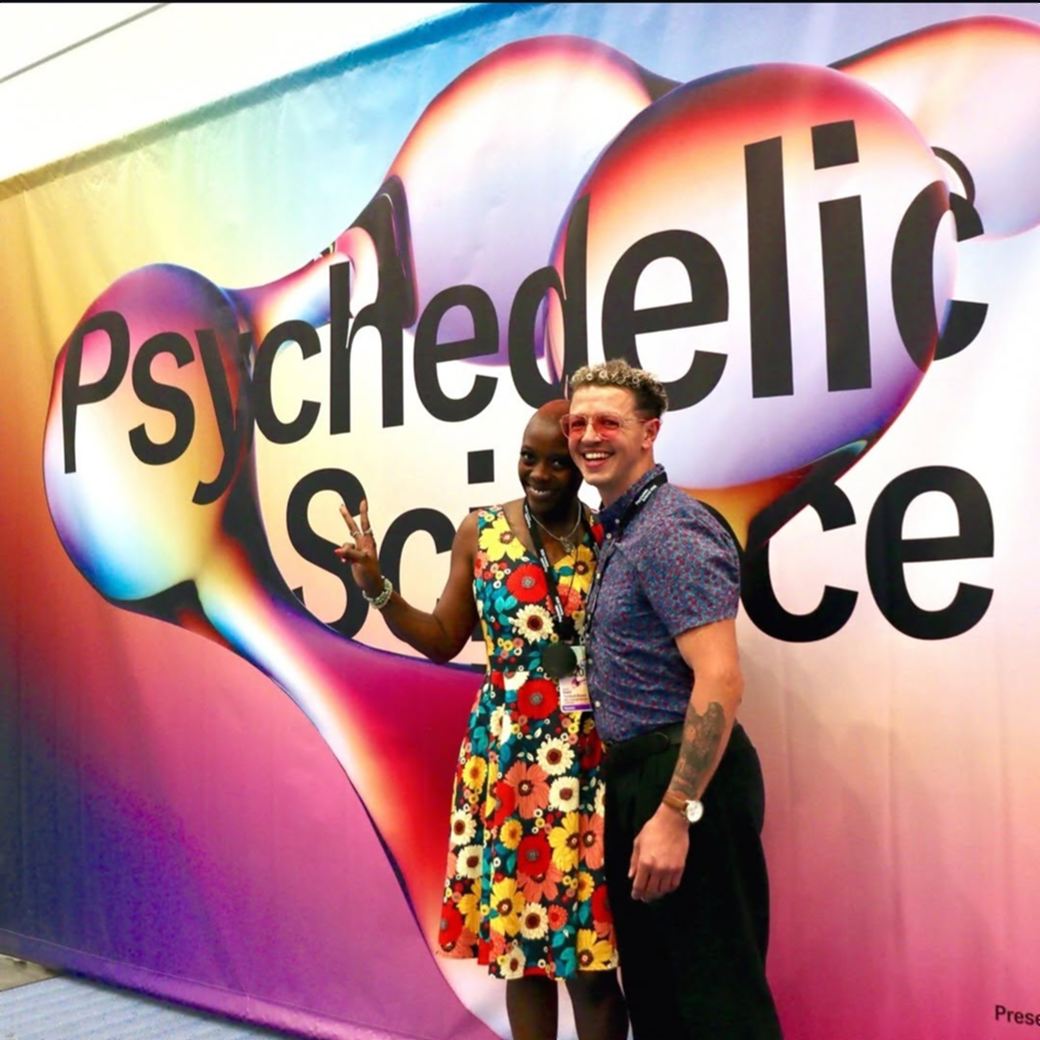 Imani and Julian posing in front of a giant Psychedelic Science conference banner.