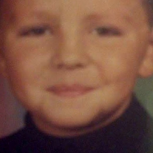 Julian Fontaine-Fox as a young boy in a dark turtleneck, smiling gently.